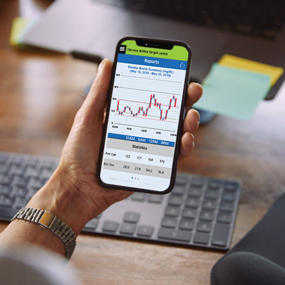 Vrouw zit aan haar bureau en controleert haar glucosewaarden in de Eversense CGM-app.