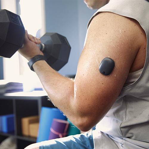Man die met gewichten sport terwijl hij een langetermijn-CGM voor diabetes draagt.
