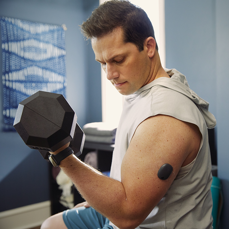 Man fitnest met gewichten en heeft een CGM-systeem op zijn arm.