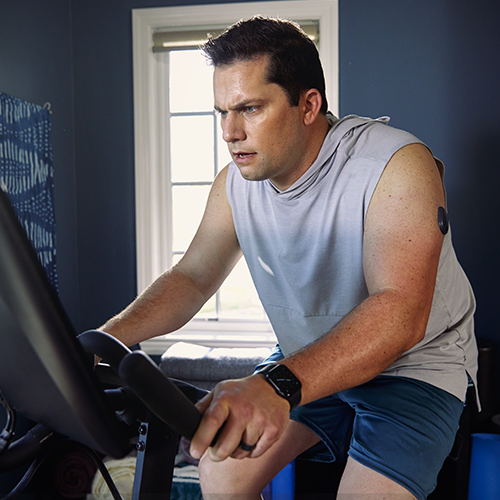 Man zit op een hometrainer terwijl hij een Eversense CGM draagt.