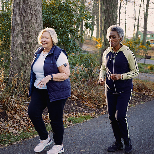 Twee vrouwen met Eversense CGM-apparaten wandelen buiten.