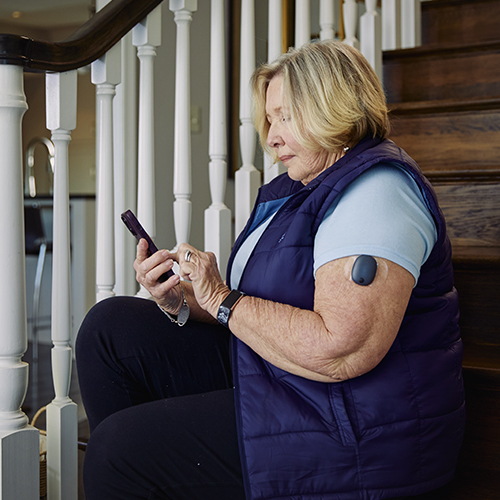 Vrouw zit op de trap terwijl ze de Eversense CGM-app gebruikt met haar geimplanteerde CGM.